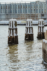 Fototapeta premium Snowy wooden piling dolphins in East River at New York. Three timber mooring posts stand in water near waterfront building.