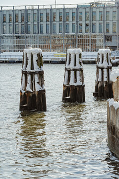 Snowy wooden piling dolphins in East River at New York. Three timber mooring posts stand in water near waterfront building.