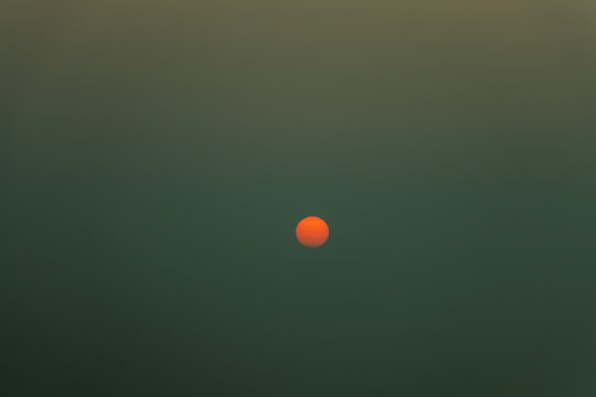 Golden sunset sun disk glowing in hazy atmosphere during late dusk.