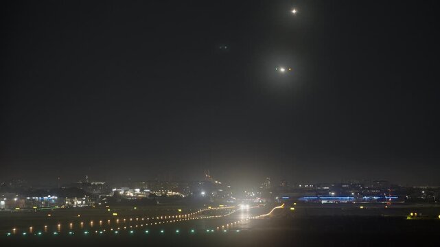 An airplane with landing lights approaches an illuminated airport runway at night as a bright lightning flash lights up dark storm clouds over the city