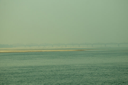 Old steel railway bridge spanning over flat sandy riverbed scenery.