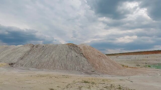 Detailed view of steep white kaolin clay slopes in an abandoned open pit quarry under a cloudy sky.