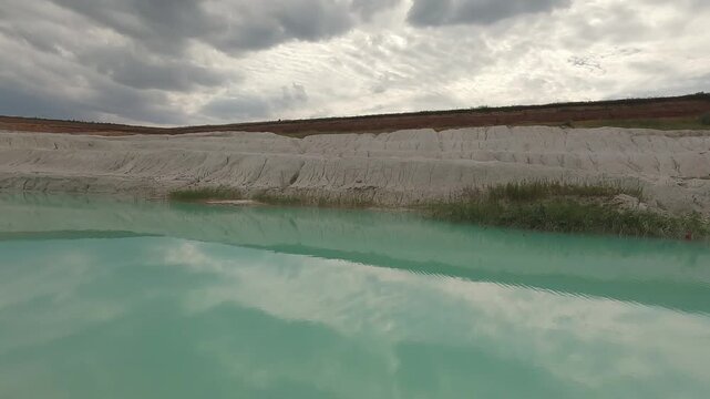 Close view of vivid turquoise water filling part of an abandoned kaolin clay quarry surrounded by pale mineral deposits.