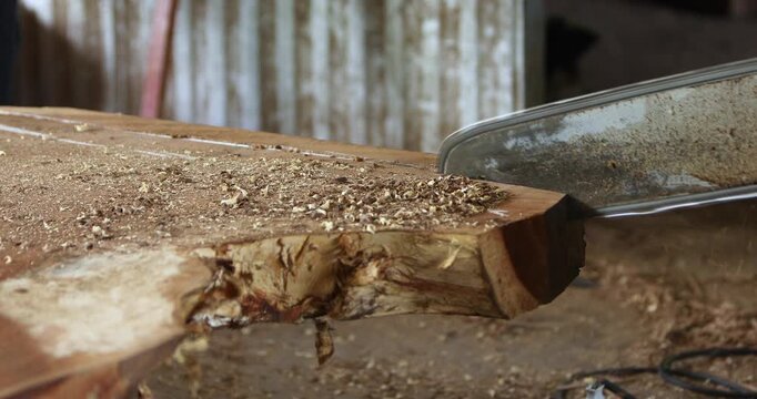 Carpenter shaping and cutting a wooden board with a power tool, creating sawdust and wood shavings in a workshop, showcasing woodworking, craftsmanship and furniture production.