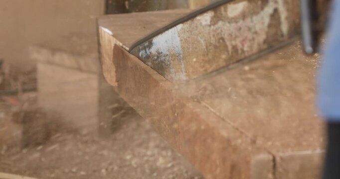 Carpenter shaping and cutting a wooden board with a power tool, creating sawdust and wood shavings in a workshop, showcasing woodworking, craftsmanship and furniture production.
