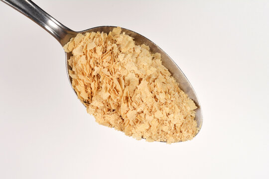 Top view of a metal tablespoon filled with dry yellow nutritional yeast flakes isolated on a clean white surface.