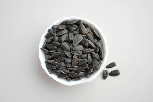 There is a small bowl with sunflower seeds on a grey background.