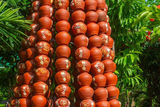Reddish-brown ceramic jars stacked in tall columns among green foliage in Bac Ninh, Vietnam, some bearing the gold Vietnamese inscription "Loc" for prosperity.