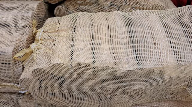 Many wooden logs inside mesh bags are piled together on a shelf, fireplace firewood supplies, cozy winter preparations, outdoor camping fuel.