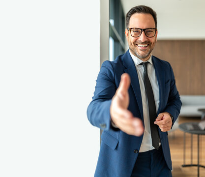 Smiling male professional extending hand for handshake, welcoming clients and showing trust, a partnership concept in a modern office environment