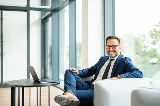 Successful male business professional, wearing glasses and a tie, sitting comfortably in an office setting with a laptop, exuding confidence and expertise in his role