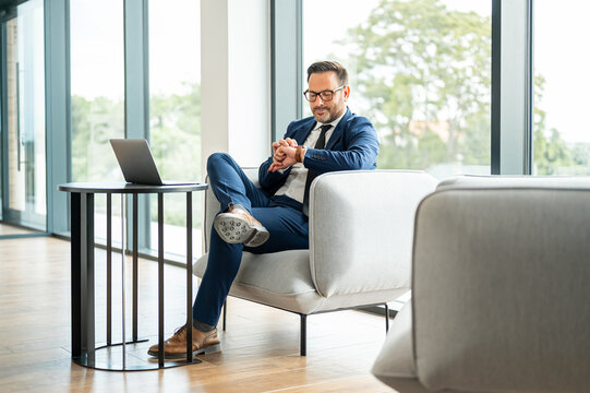 Businessman sitting comfortably in a modern office lounge, looking at his timepiece, symbolizing punctuality, time management, and readiness for business appointments