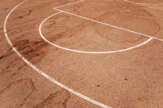 High angle view of white painted game lines on a reddish-brown asphalt outdoor basketball court surface.