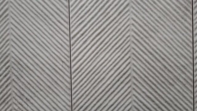 Textured ceramic tile wall with grey and white chevron herringbone pattern creates modern background. Interior architectural finishes, contemporary home design materials, geometric abstract textures.