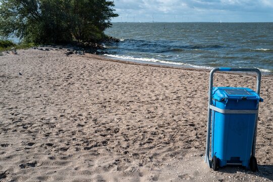 Trash bin stands on sandy beach near water under cloudy sky in coastal area