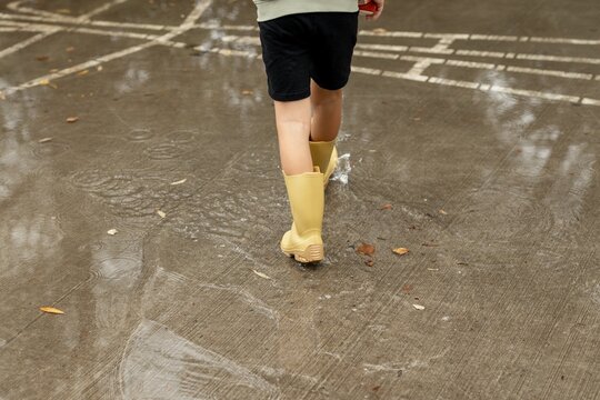 Child Wearing Yellow Rain Boots on Wet Pavement