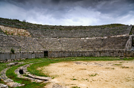 Curved stone seating tiers of the Ancient Theatre of Dodona under dramatic storm sky in Greece
