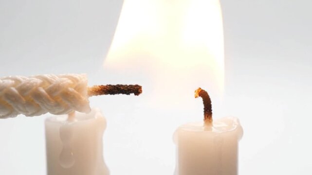 Lit candle wick igniting a second candle against a white background