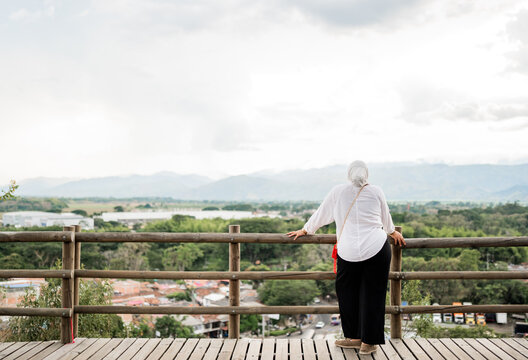 Mujer mayor contemplando paisaje monta&ntilde;oso desde mirador de madera en Colombia
