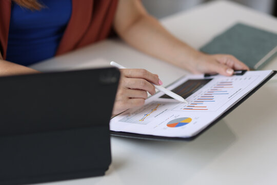 Businesswoman sitting at desk is analyzing financial charts and graphs, indicating on business performance and data analysis.