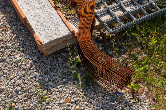 Steel rebar, welded reinforcement mesh and a precast concrete lintel stored on gravel at a construction site, showing structural building materials prepared for masonry and concrete work.