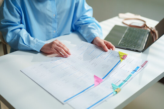 Legal counsel examining complex contractual agreements and corporate schedules beside an open laptop in a sunlit workspace, contract lifecycle management, due diligence, and legal compliance workflows