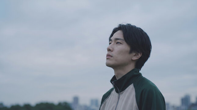 曇り空を見上げるアンニュイな表情の若い男性学生と進路や就職の不安