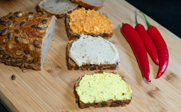 Slices of whole-grain bread with sunflower seeds and various types of cream cheese. read, food, baked goods, grains or wheat product, vegetarian food, cutting board in the kitchen.
