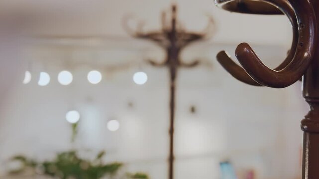 Close up of wooden coat rack with multiple hooks in soft lighting. hand briefly places item on one hook demonstrating interaction within scene. background features blurred interior elements