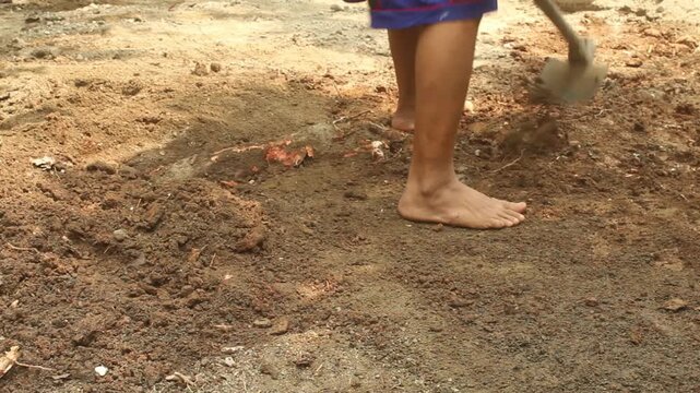 Man manually leveling and preparing soil with a traditional hoe during outdoor pond construction and land preparation.