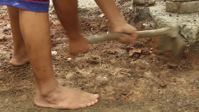 Man using a traditional hoe to dig and expand a pond area in soil, showing manual excavation and outdoor land preparation.
