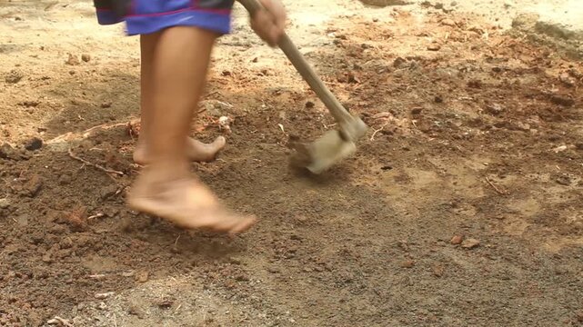 Man manually leveling and preparing soil with a traditional hoe during outdoor pond construction and land preparation.