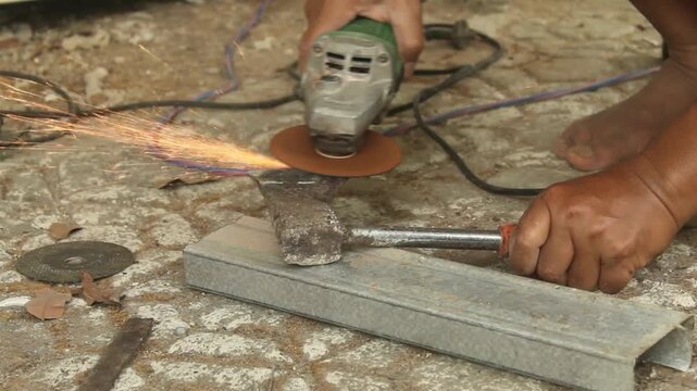 Man sharpening an axe blade with an angle grinder, producing sparks during metal grinding and tool maintenance in an outdoor work area.
