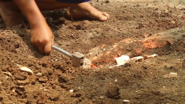 Man chopping a tree root with an axe after digging into the soil during outdoor land clearing and manual ground preparation.