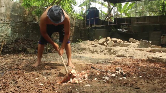Man using a metal crowbar to pry and remove a tree root from the soil during outdoor land clearing and manual ground preparation