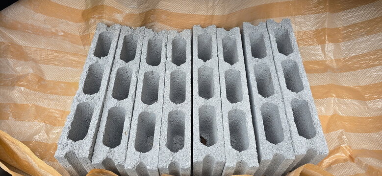 Eight hollow concrete blocks are placed on Orange and white PE tarpaulin. These are construction materials made from cement and sand, molded into rectangular blocks with hollow center. Plastic tarp
