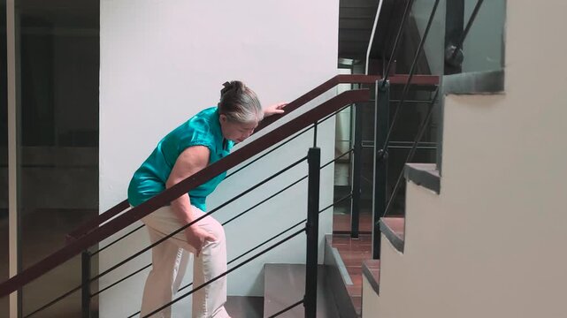 60s old senior asian woman slowly climbing staircase with knee joint pain or leg muscle atrophy, indoor home scene during daytime, health and body care and elderly mobility concept, side view