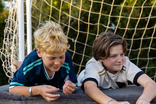 young boys smiling , lying down with soccer net in background at sunset