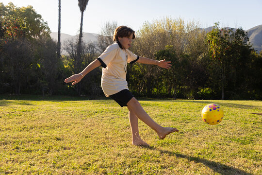teenage boy kicking soccer ball on field