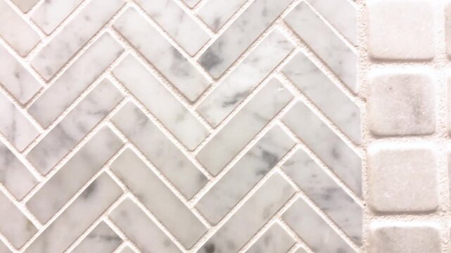 Natural stone marble tile wall transition from herringbone pattern to square block texture closeup.