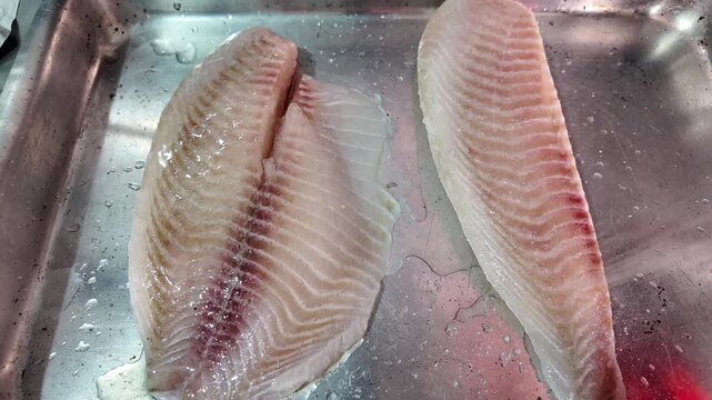 Two fresh tilapia fish fillet in a stainless steel container, ready for cooking
