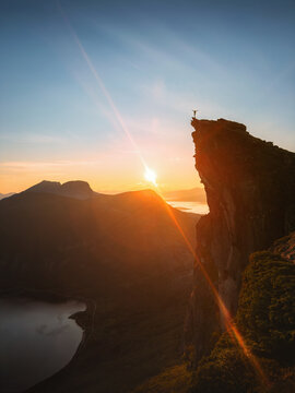 Brave hiker standing on Kjerna cliff edge travel solo in Norway at sunset mountain hiking extreme adventure outdoor, freedom achievement summit active vacations wilderness exploration midnight sun