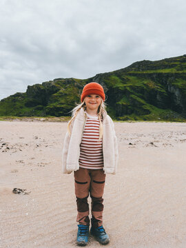 Cute girl tourist standing on remote beach in Norway family travel outdoor adventure hiking vacation active lifestyle, exploration nature eco tourism scandinavian destination childhood candid emotions