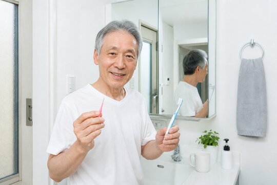 洗面所で歯間ブラシと歯ブラシを持つシニア男性