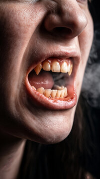 Vampire fangs visible in open mouth of snarling woman. Horror concept with smoke and sharp teeth.