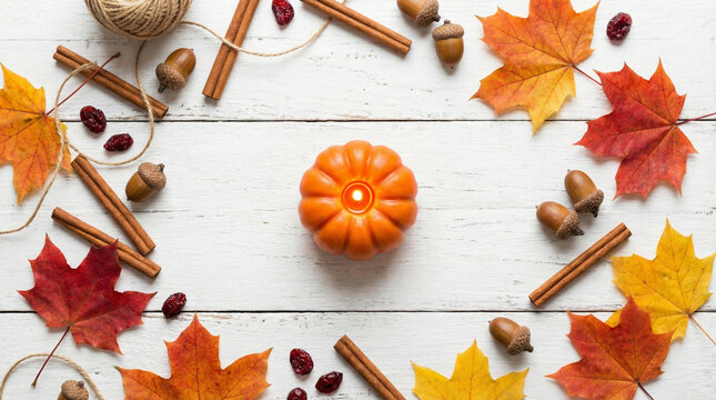 Minimalist Fall Flat Lay with Pumpkin Candle and Dried Leaves. Clean overhead arrangement of small pumpkin candle, cinnamon sticks, acorns and scattered maple leaves on white wooden surface