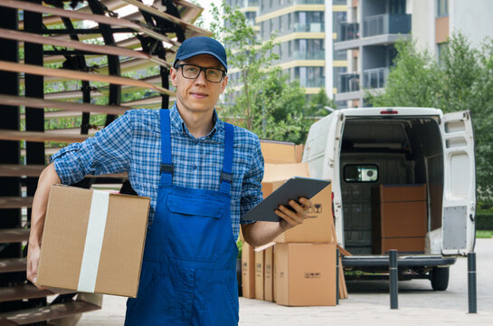 A courier holding a cardboard box and digital tablet with a delivery van in the background.