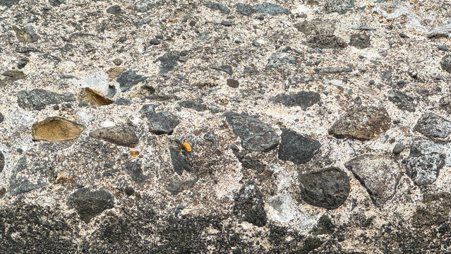 Close-up of weathered rough concrete wall with embedded natural grey and brown stones texture