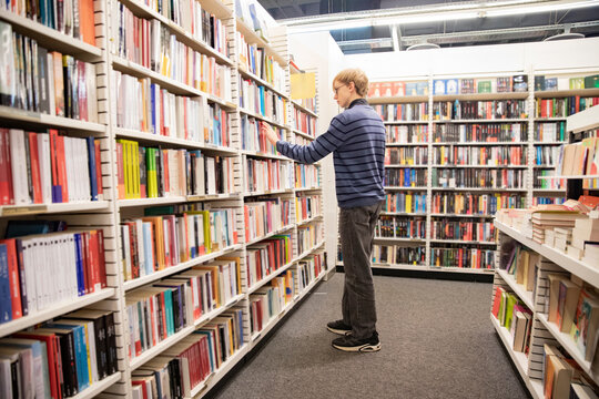 young student searching literature in long row of bookshelves in big library
