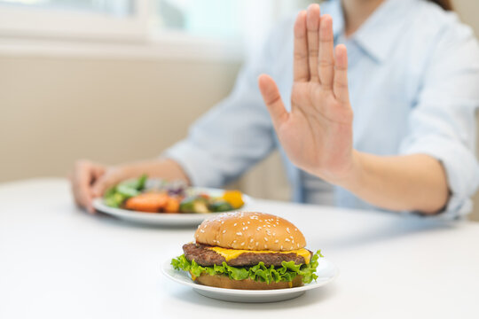 Diet concept, asian young woman hand reject eat burger, hamburger on plate, push out or deny to eat fast, junk food choose green vegetable salad, girl eat low fat for good healthy, getting weight loss